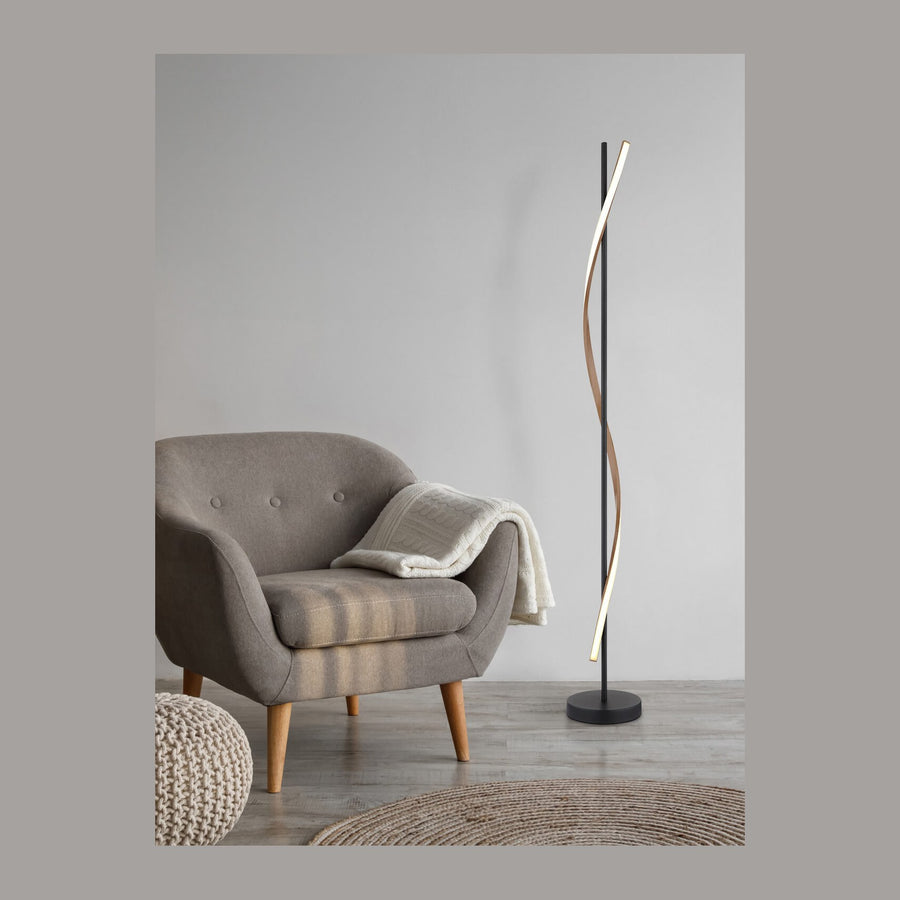 Lampadaire noir mat et ruban lumineux torsadé dans un salon gris avec fauteuil.