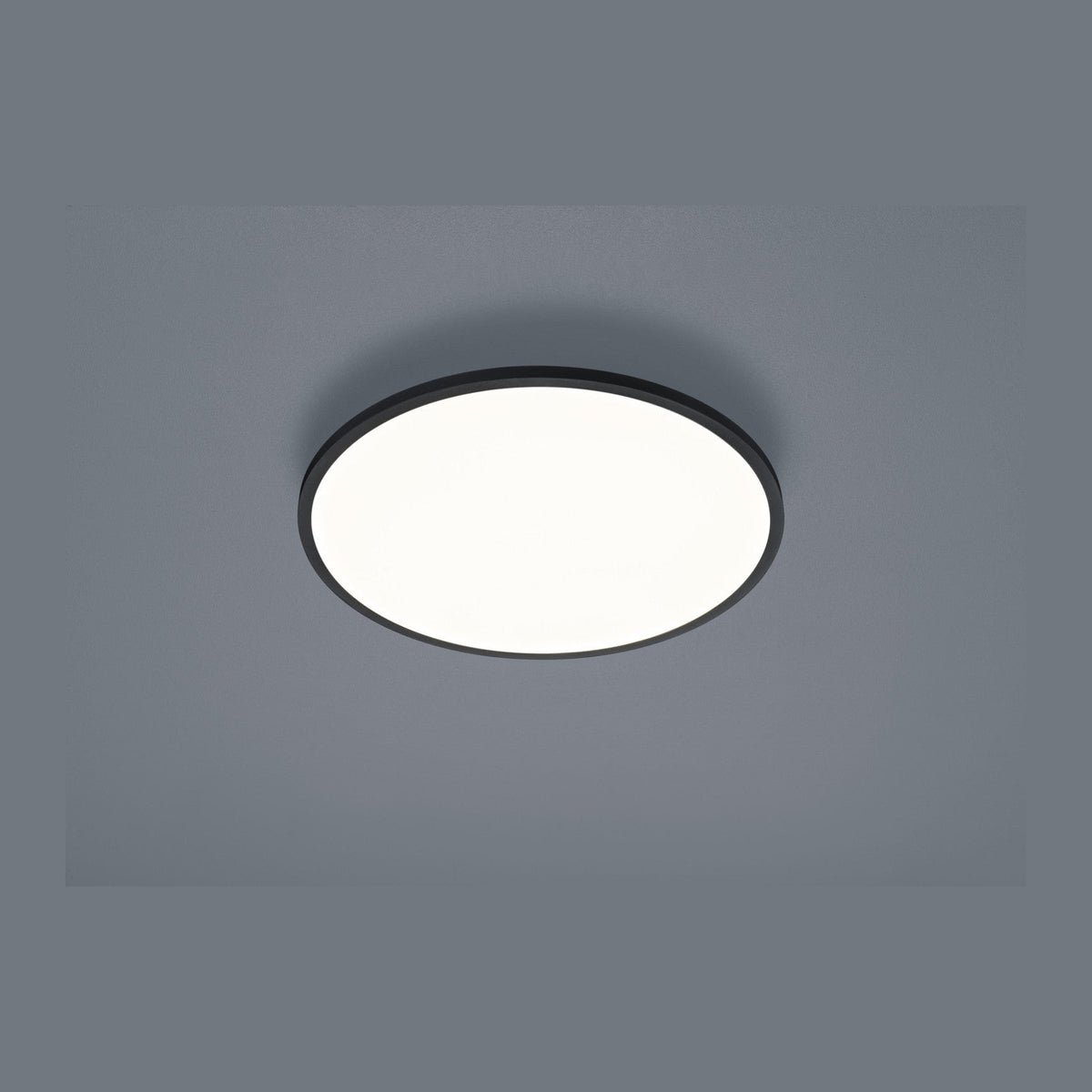 Plafonnier rond noir vu de face, diffuseur blanc allumé sur fond gris uni