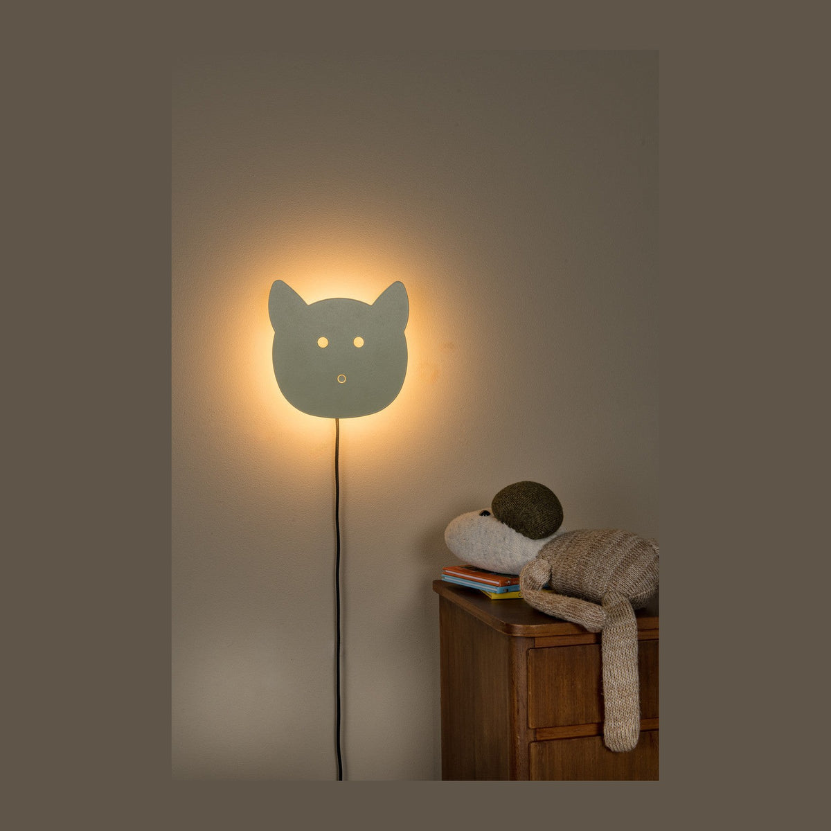 Applique murale en forme de tête de chat allumée, câble pendant, commode en bois et peluche.