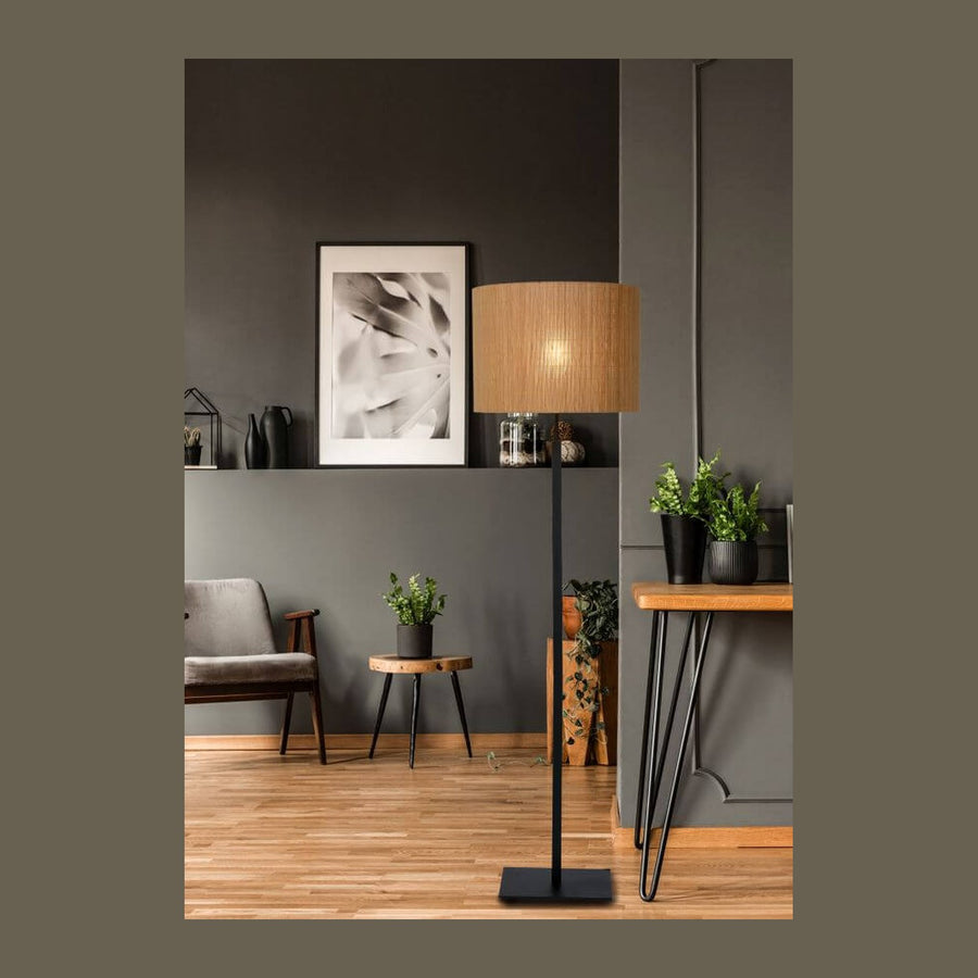 Lampadaire noir à abat-jour rotin clair dans un salon gris avec fauteuil et plantes.