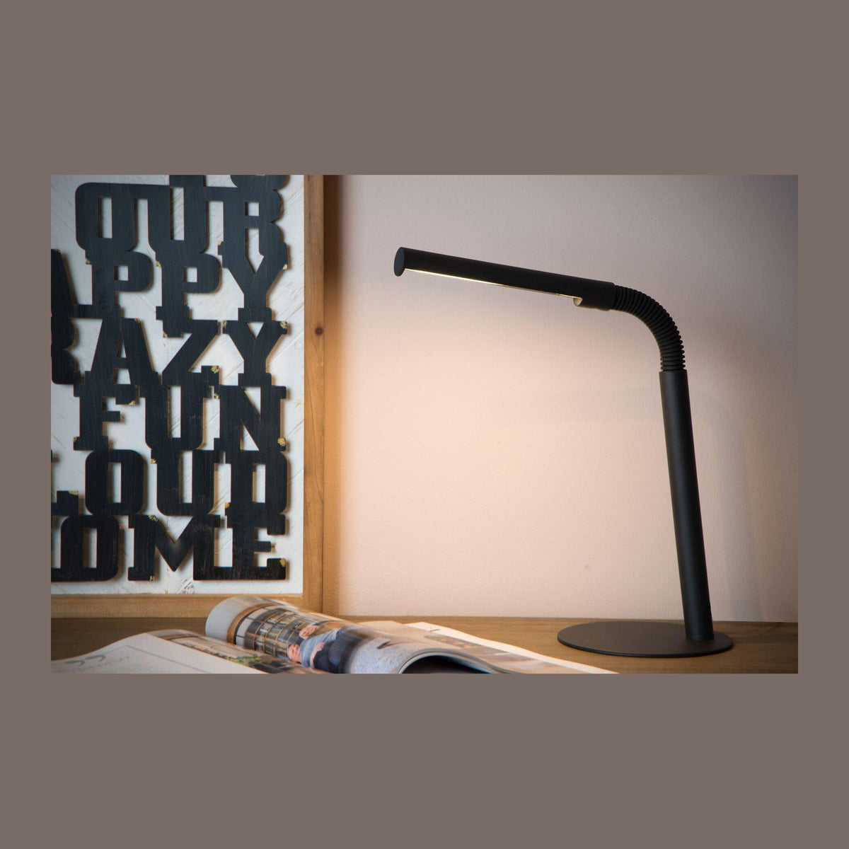 Lampe de bureau noire allumée posée sur un bureau en bois avec magazine