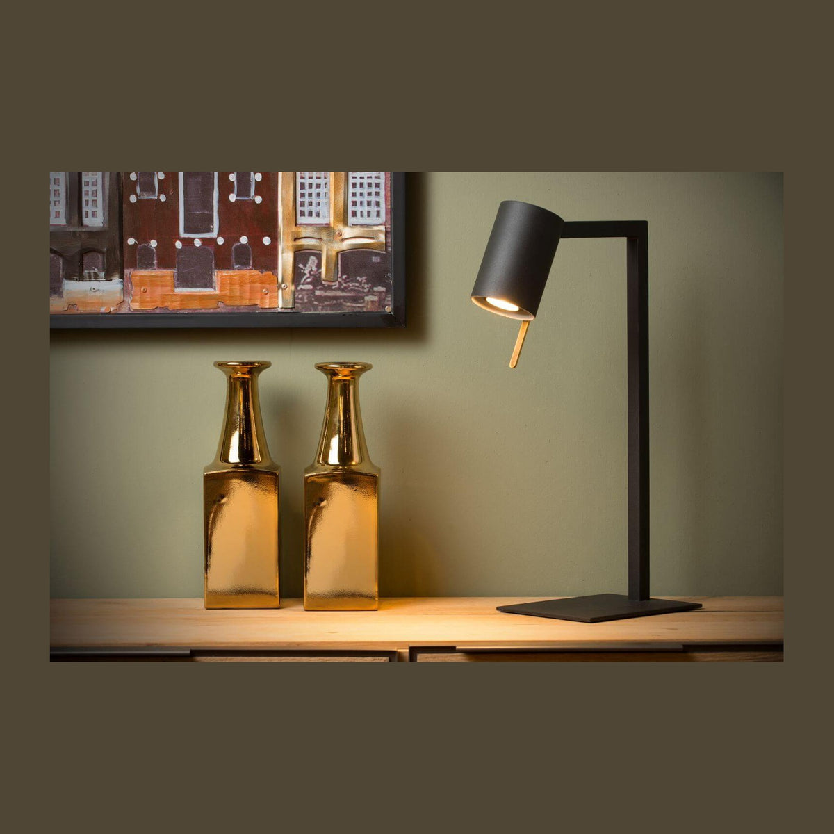 Lampe de bureau noire allumée sur un meuble en bois, avec deux vases dorés.