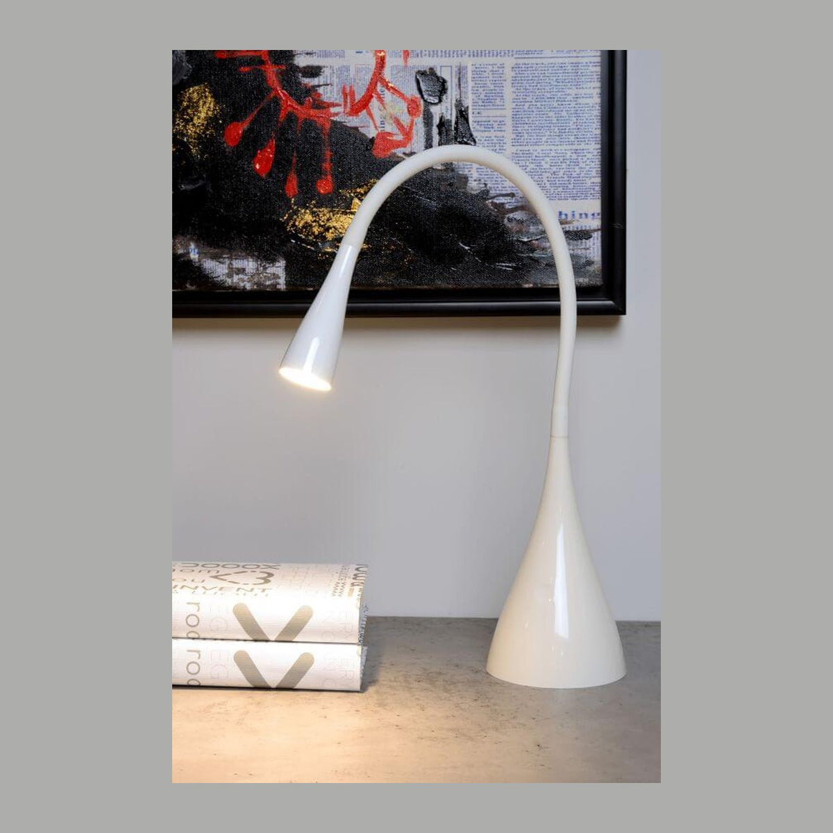 Lampe de bureau blanche allumée posée sur une console en béton devant un tableau