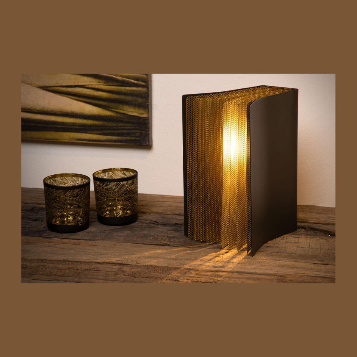 Lampe noire et dorée posée sur table en bois, deux photophores et tableau au mur.