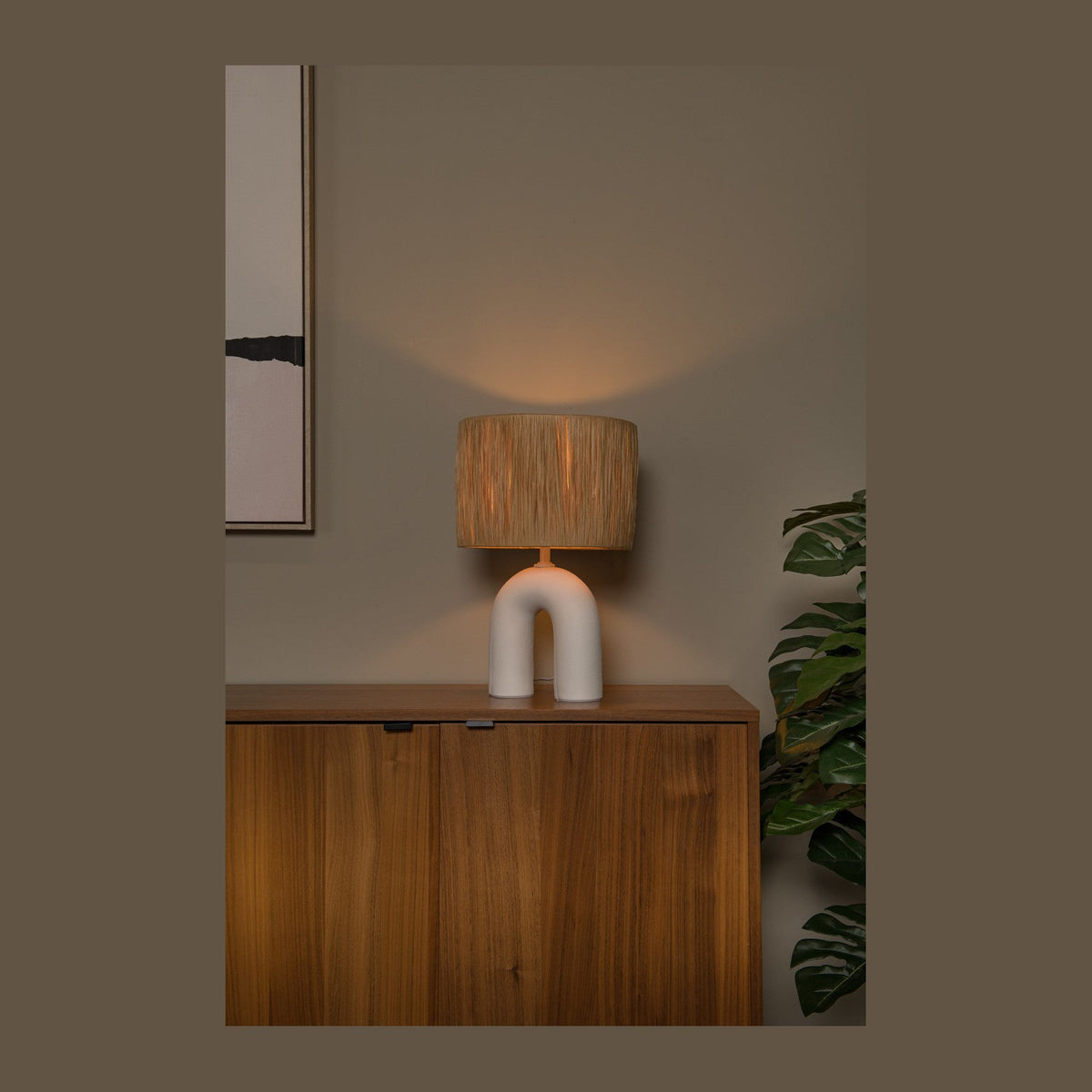 Lampe posée sur un buffet en bois, éclairant un mur beige en ambiance chaleureuse