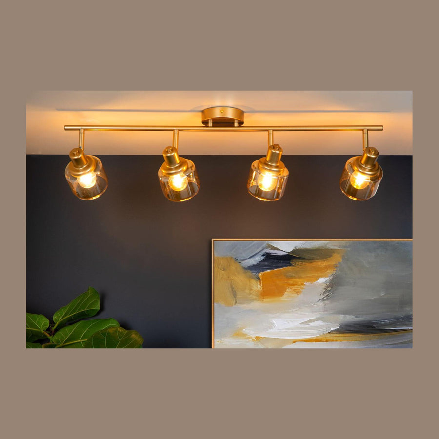Plafonnier doré à quatre lumières allumé devant un mur sombre et un tableau abstrait.