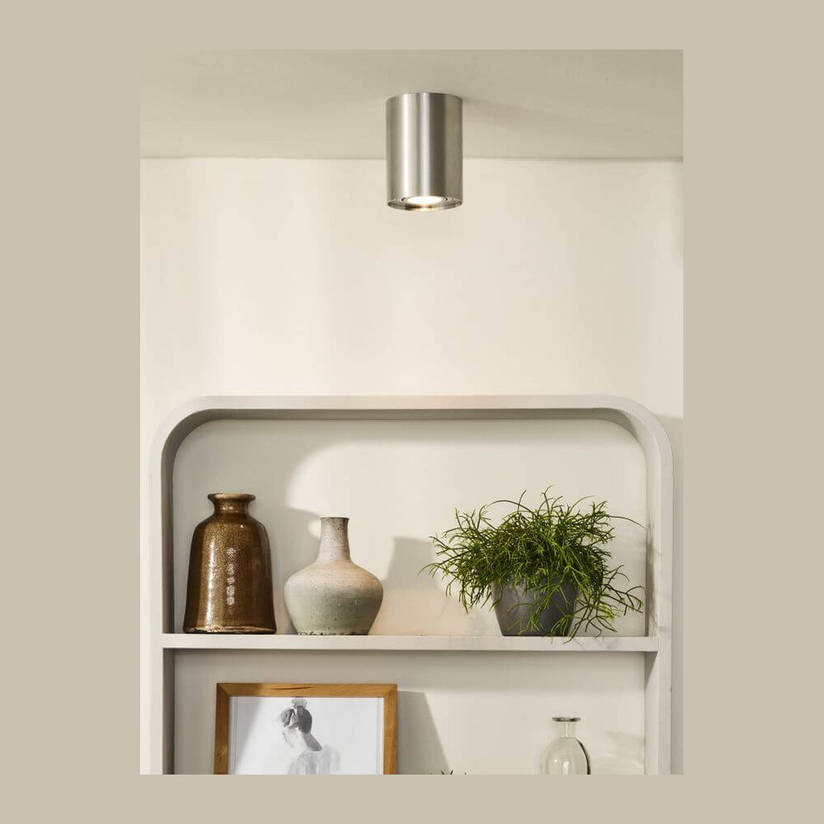 Plafonnier cylindrique chromé fixé au plafond, au-dessus d'une étagère blanche décorée de vases