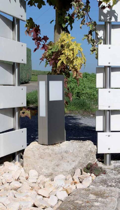 Luminaire installé sur une pierre dans un jardin, entouré de graviers et de feuillage.
