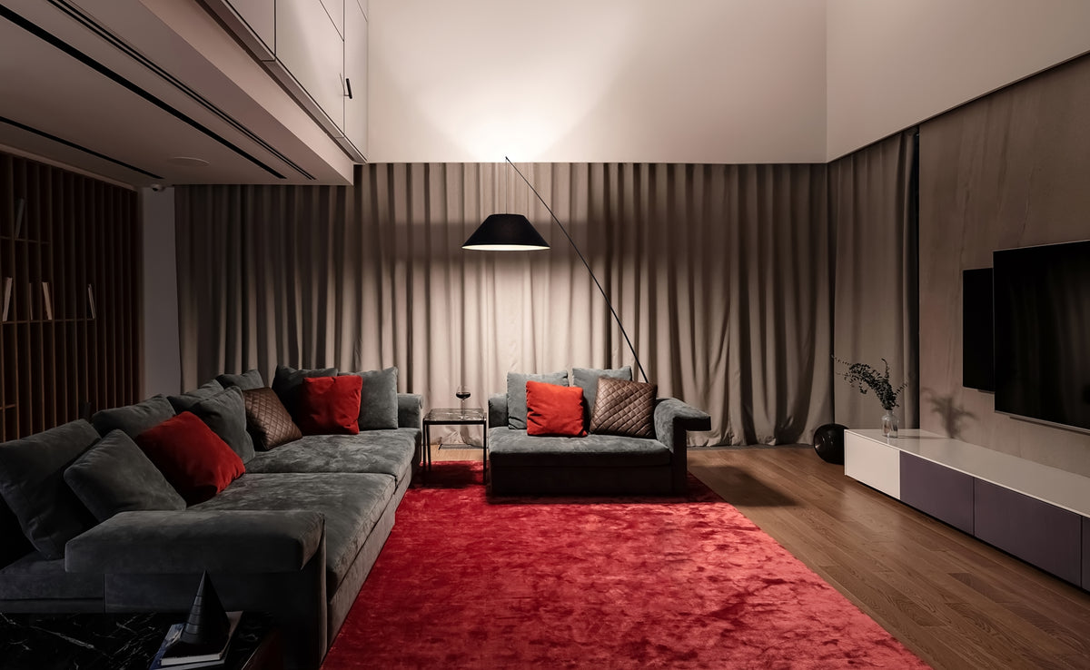 Mise en ambiance du lampadaire noir dans un salon, canapés gris et tapis rouge.
