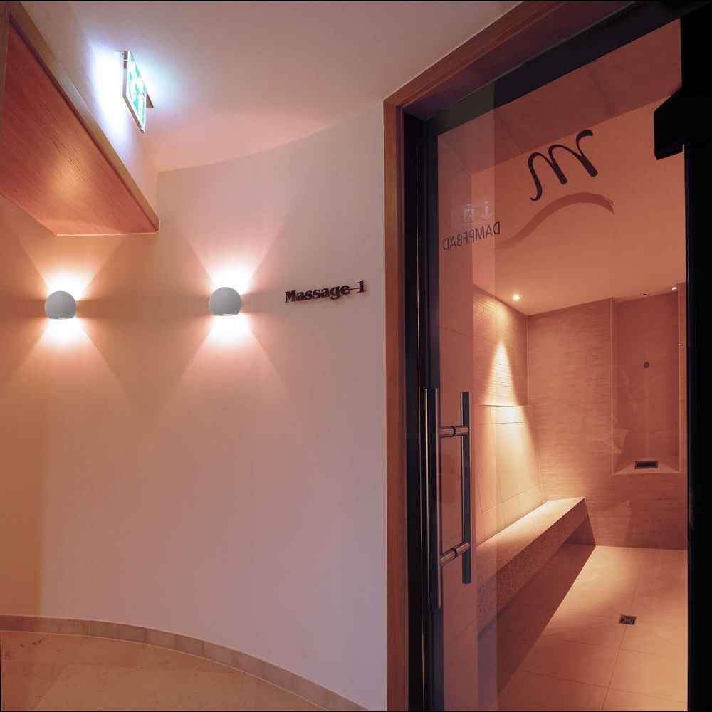 Deux appliques murales en béton éclairent un couloir de spa près d'une porte vitrée.