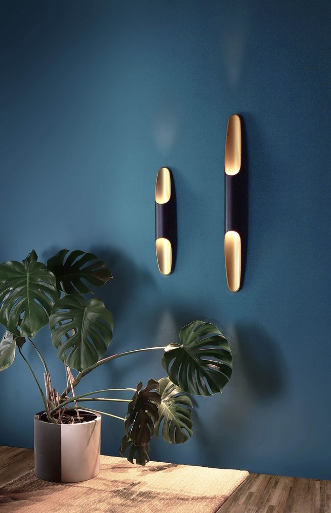 Mise en ambiance sur mur bleu avec deux appliques allumées et plante verte