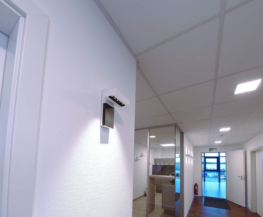 Spot blanc installé sur un mur de couloir, éclairant le panneau mural.