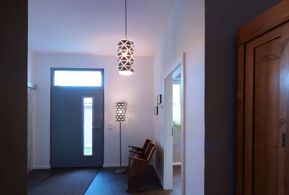 Suspension allumée dans une entrée, au-dessus d’un sol sombre et près d’une porte.