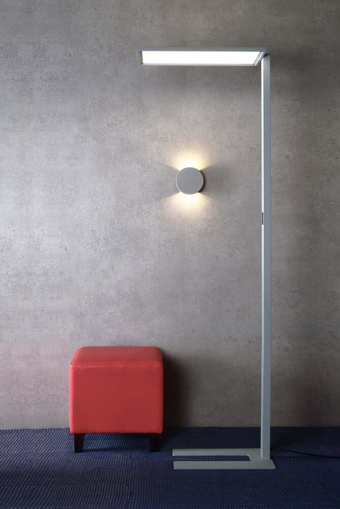 Mise en ambiance près d'un mur béton, avec pouf rouge et applique murale allumée.