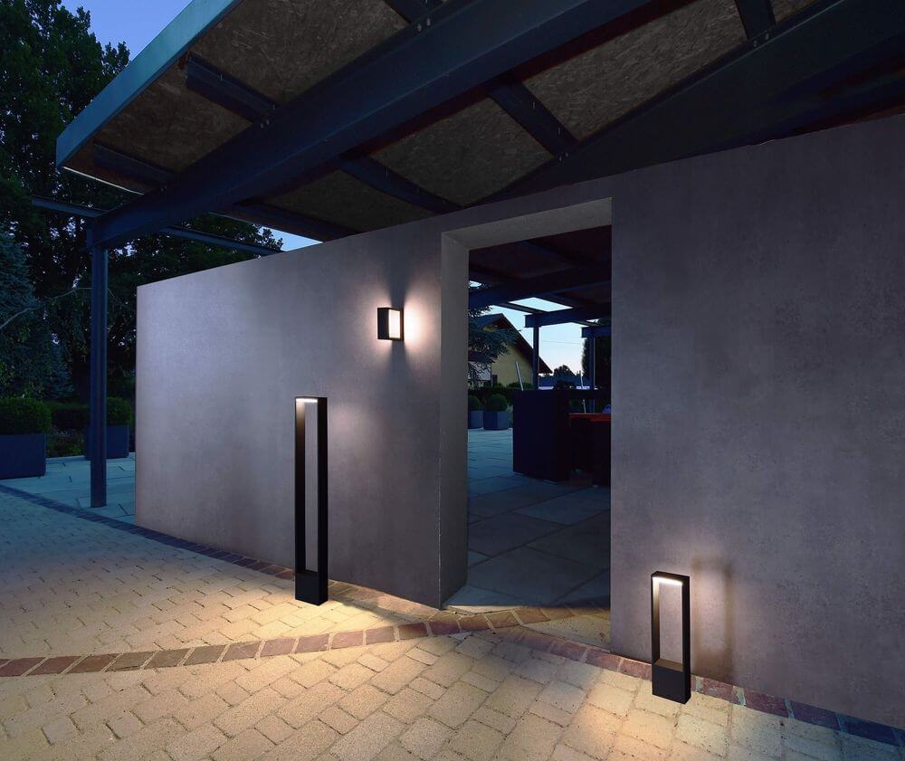 Mise en ambiance nocturne avec deux lampadaires extérieurs au sol éclairant terrasse et mur.