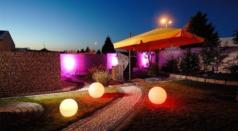 Jardin nocturne avec trois sphères lumineuses alignées le long d’un chemin gravelé.