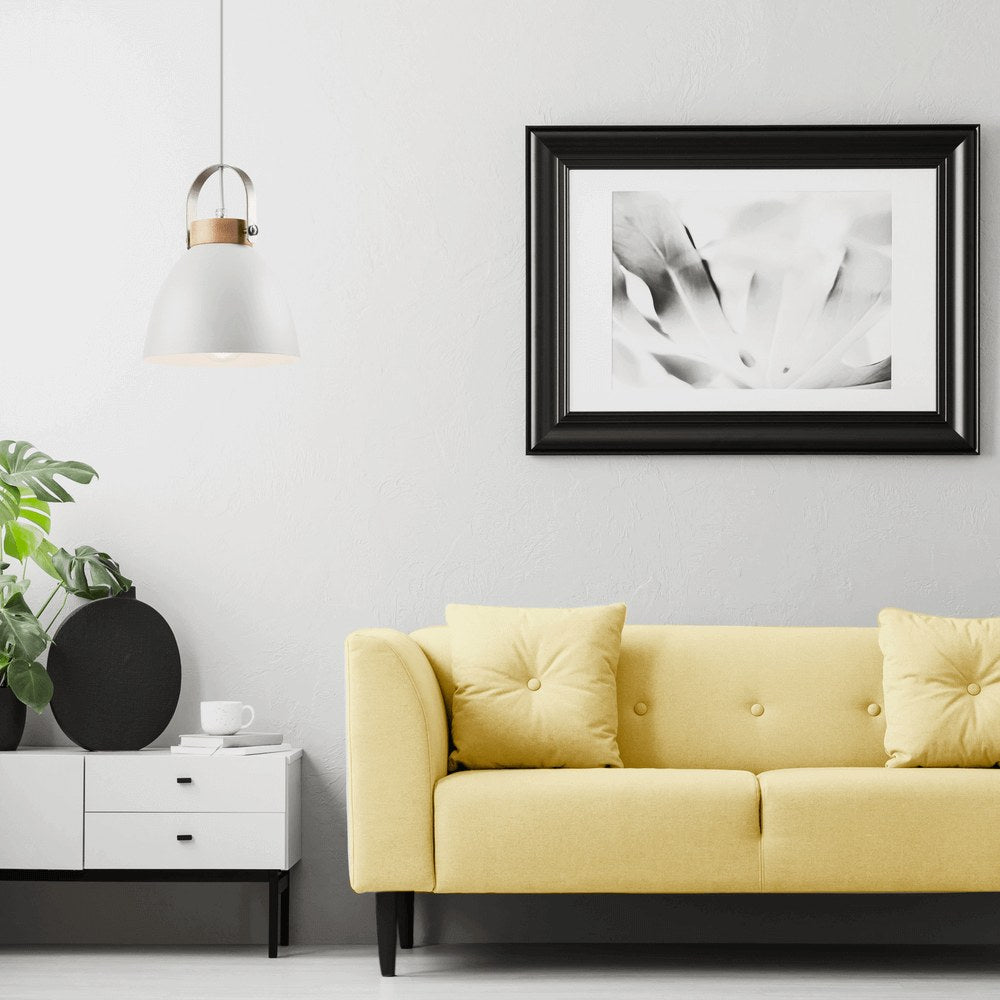 Scène de salon avec canapé jaune, cadre noir et suspension blanche suspendue.