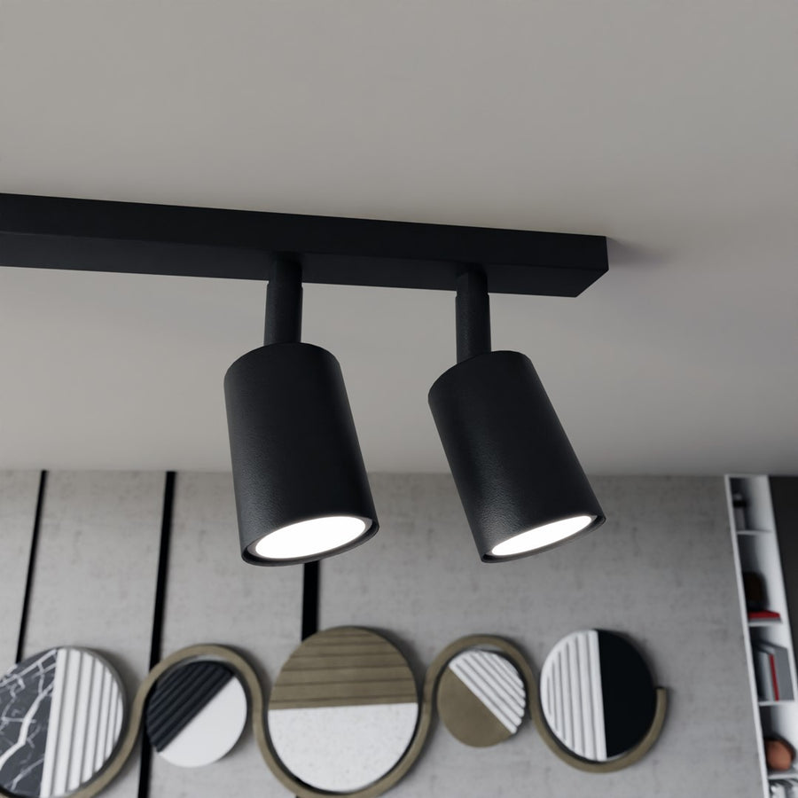 Détail rapproché de deux spots cylindriques noirs texturés sous le rail, lumière allumée.