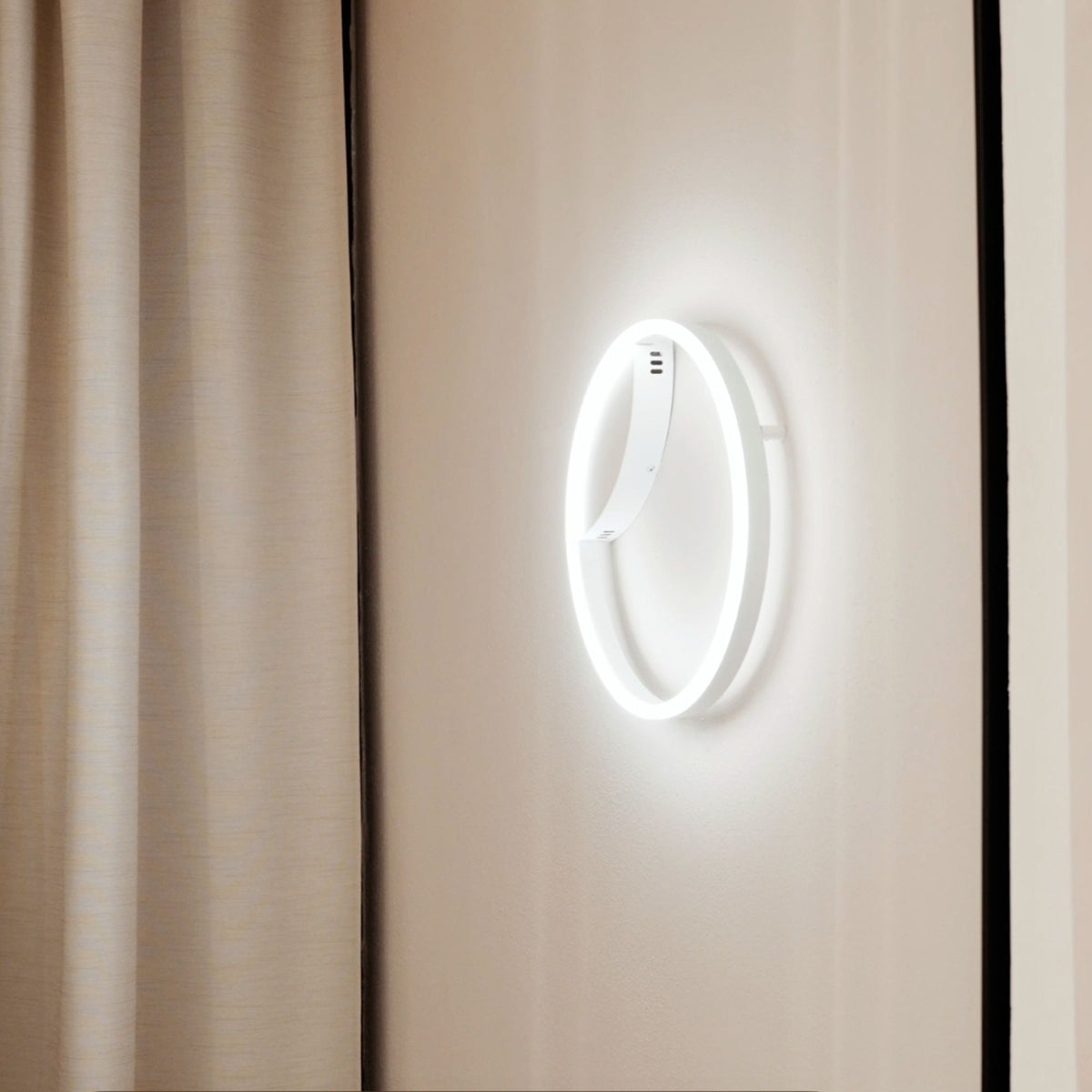Applique murale blanche en anneau LED allumée près d'un rideau beige