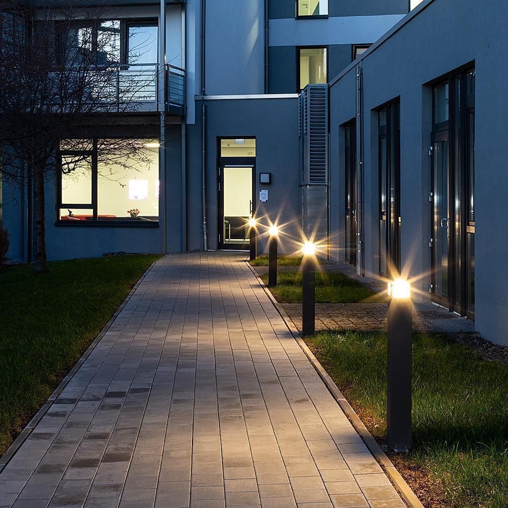 Plusieurs bornes éclairent une allée pavée le soir, halos lumineux en étoile.