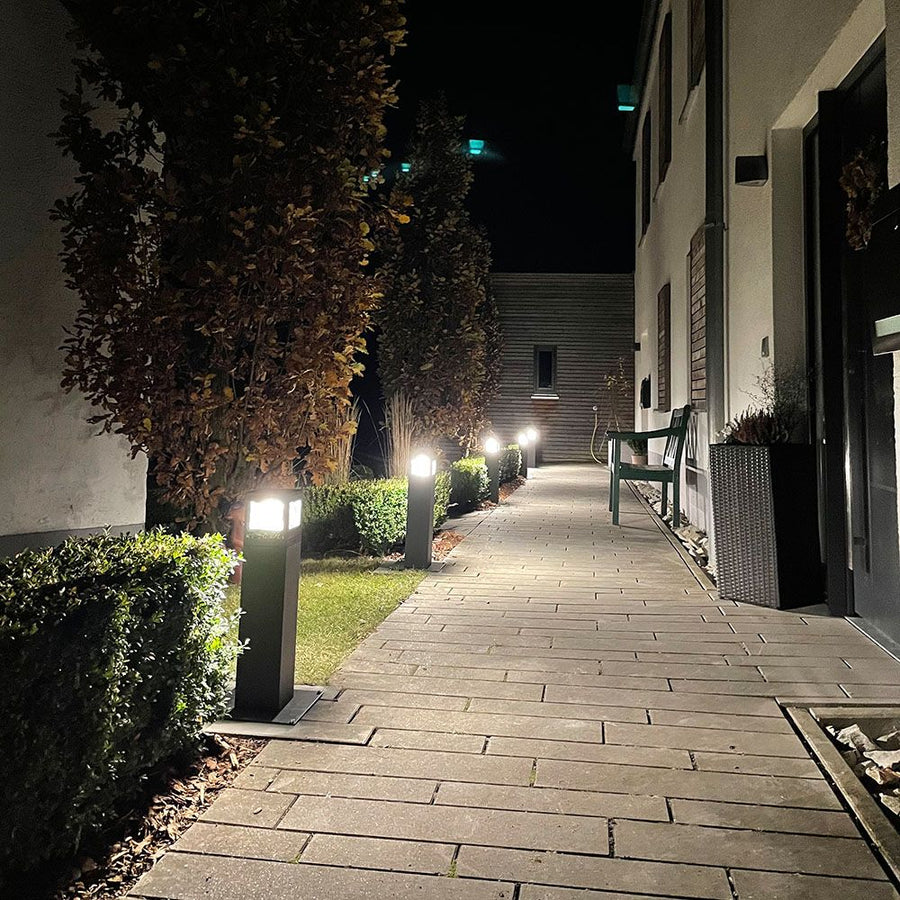 Allée pavée de nuit bordée de bornes lumineuses éclairant jardin et façade