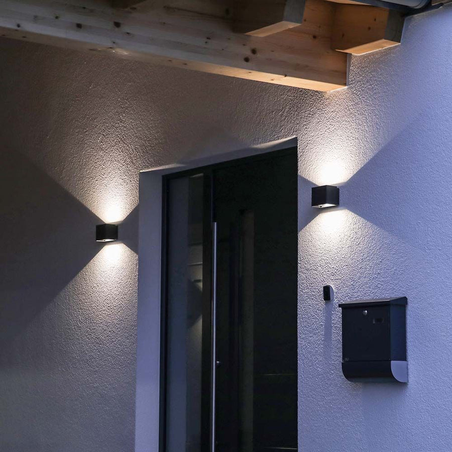 Entrée extérieure de nuit, appliques sombres de part et d'autre d'une porte vitrée.