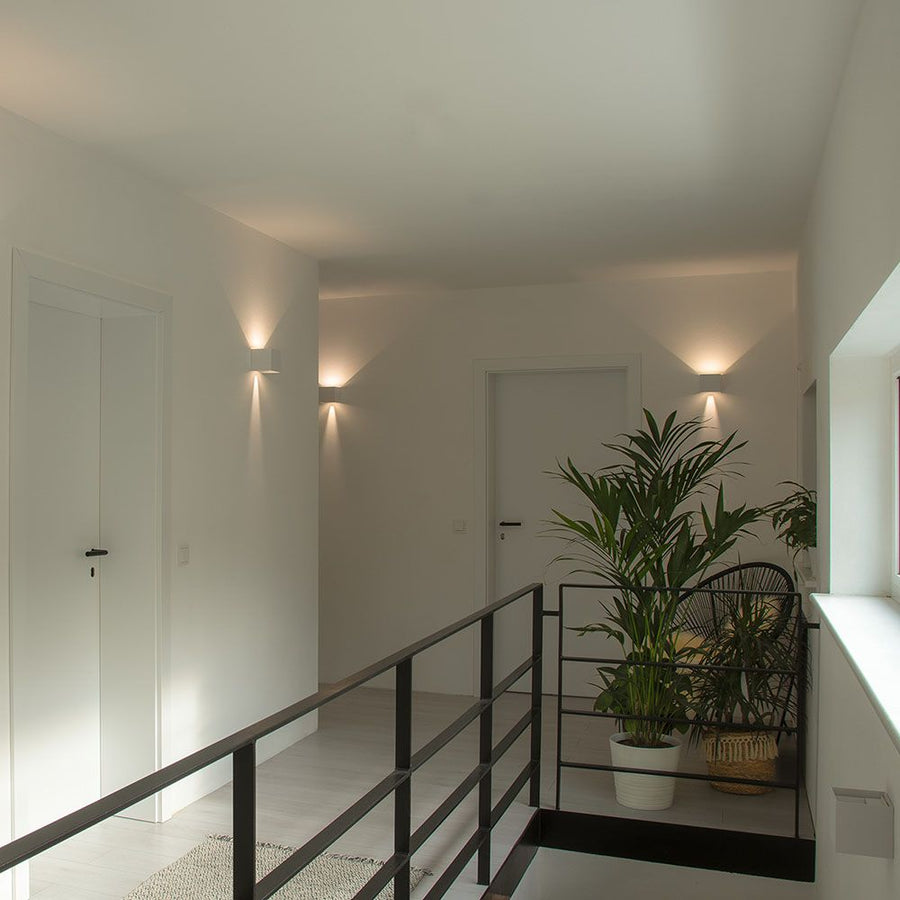 Vue plus large du couloir, appliques murales éclairant murs et plantes.