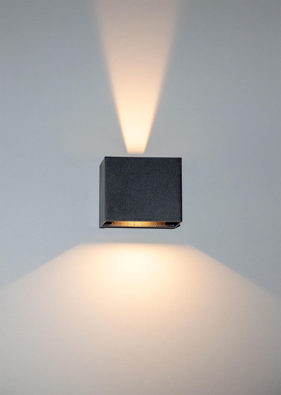 Détail de face d'une applique noire allumée, faisceau lumineux vers le haut et le bas.