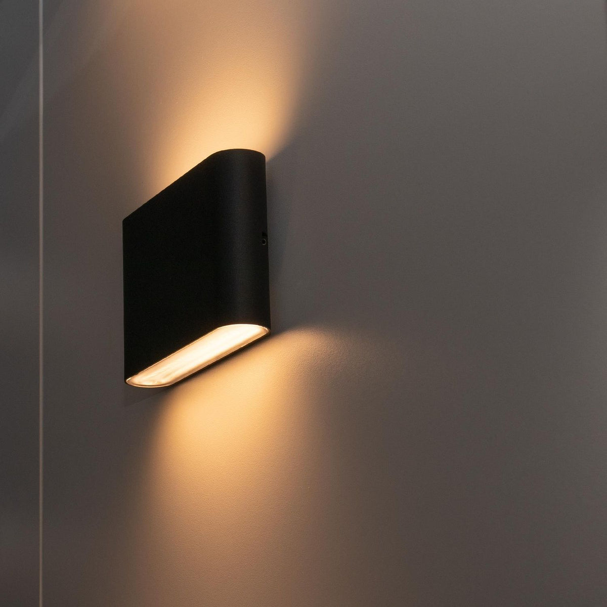 Mise en ambiance d'une applique noire allumée sur mur gris.