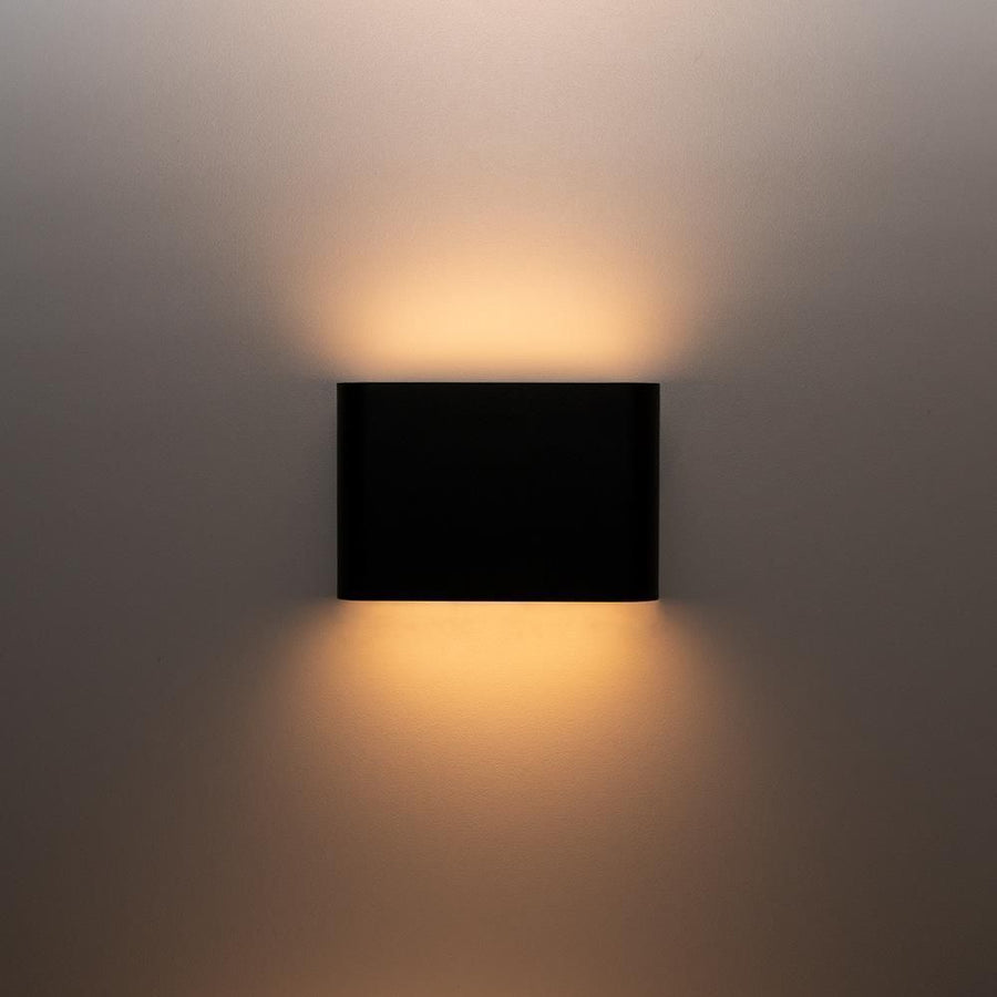 Applique noire allumée projetant deux faisceaux lumineux sur mur.