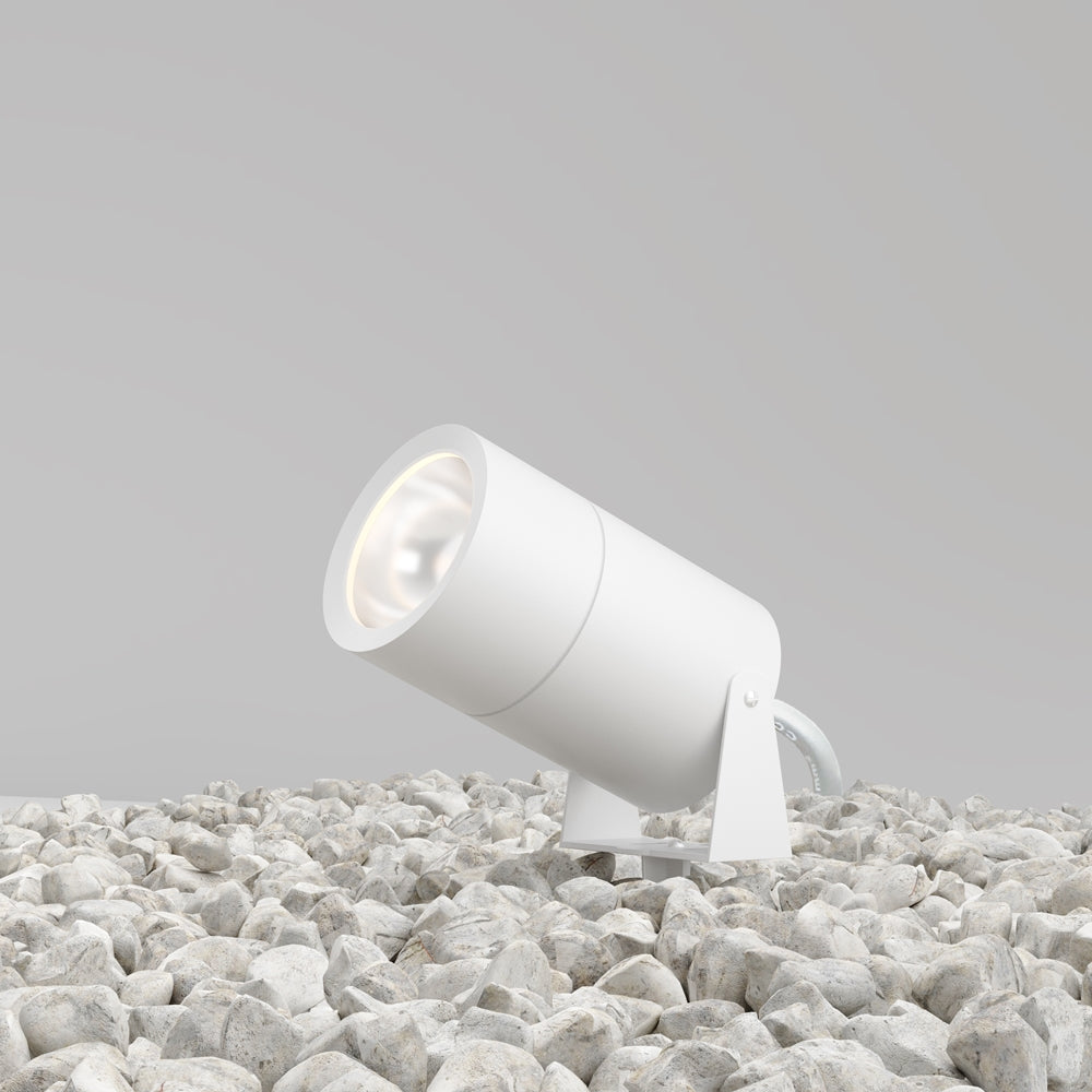 Projecteur blanc incliné posé sur un lit de galets clairs, vue d'ensemble