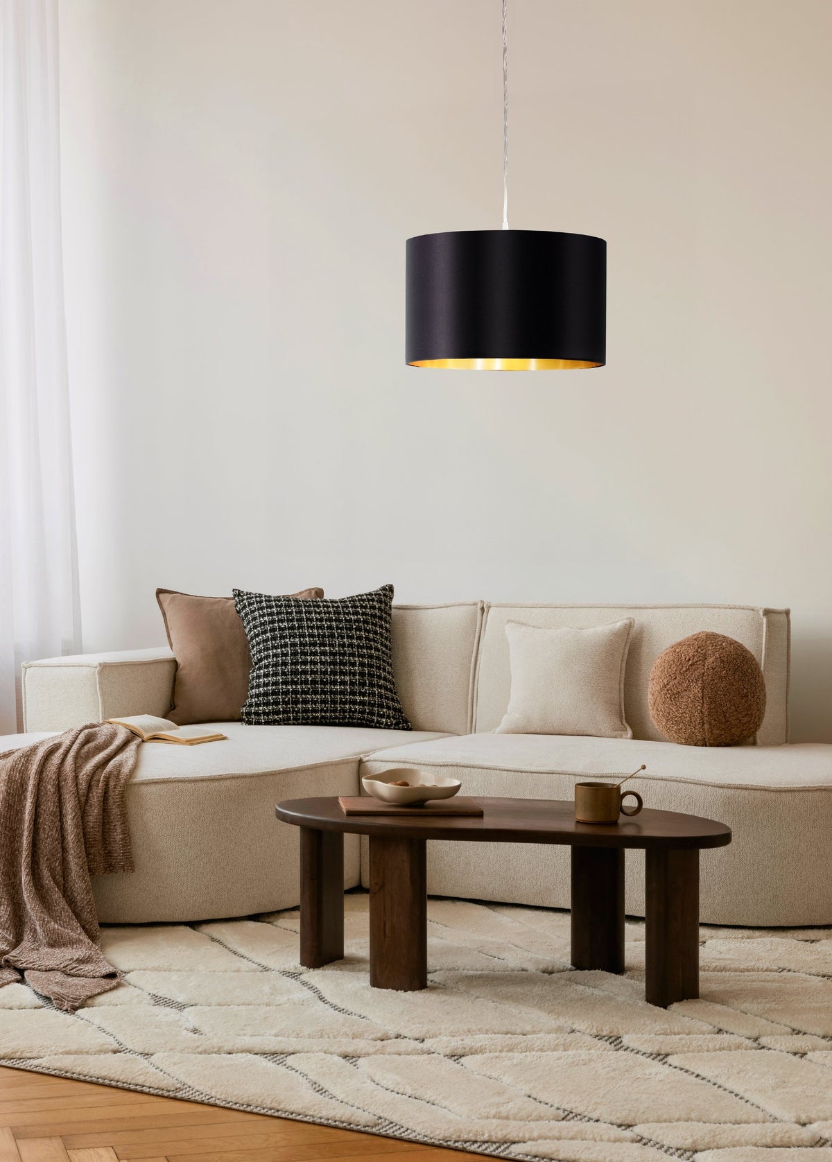 Mise en ambiance dans un salon beige, suspension allumée au-dessus du canapé et table basse