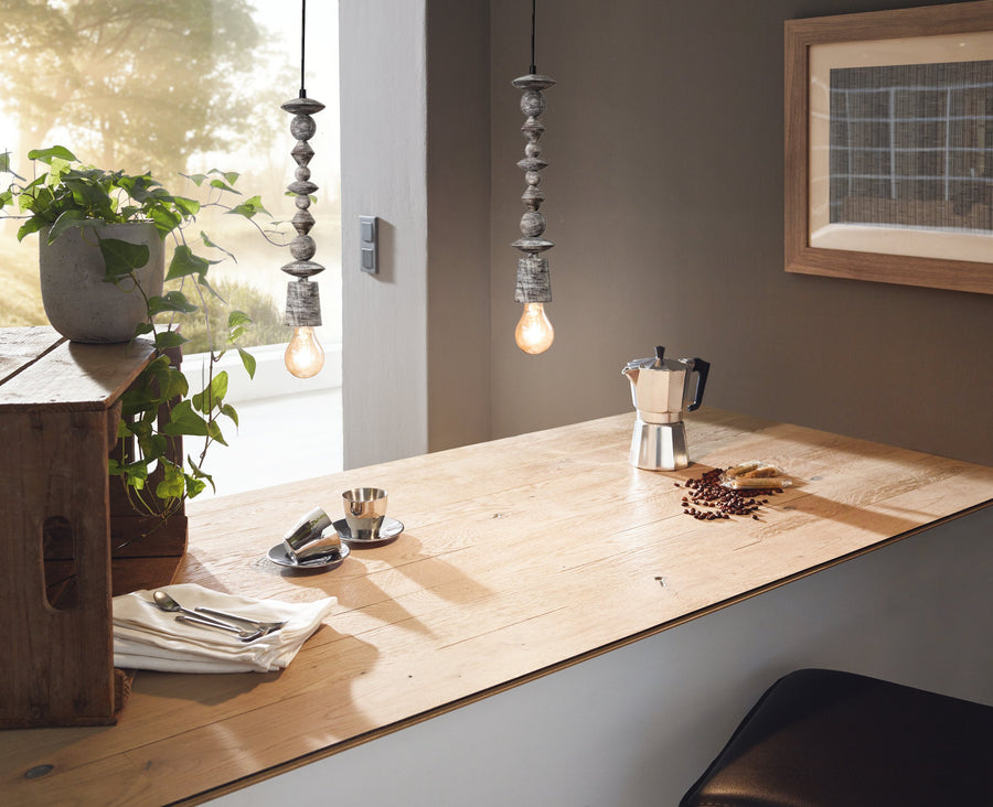 Deux suspensions éclairant un plan de travail en bois avec cafetière italienne et grains de café