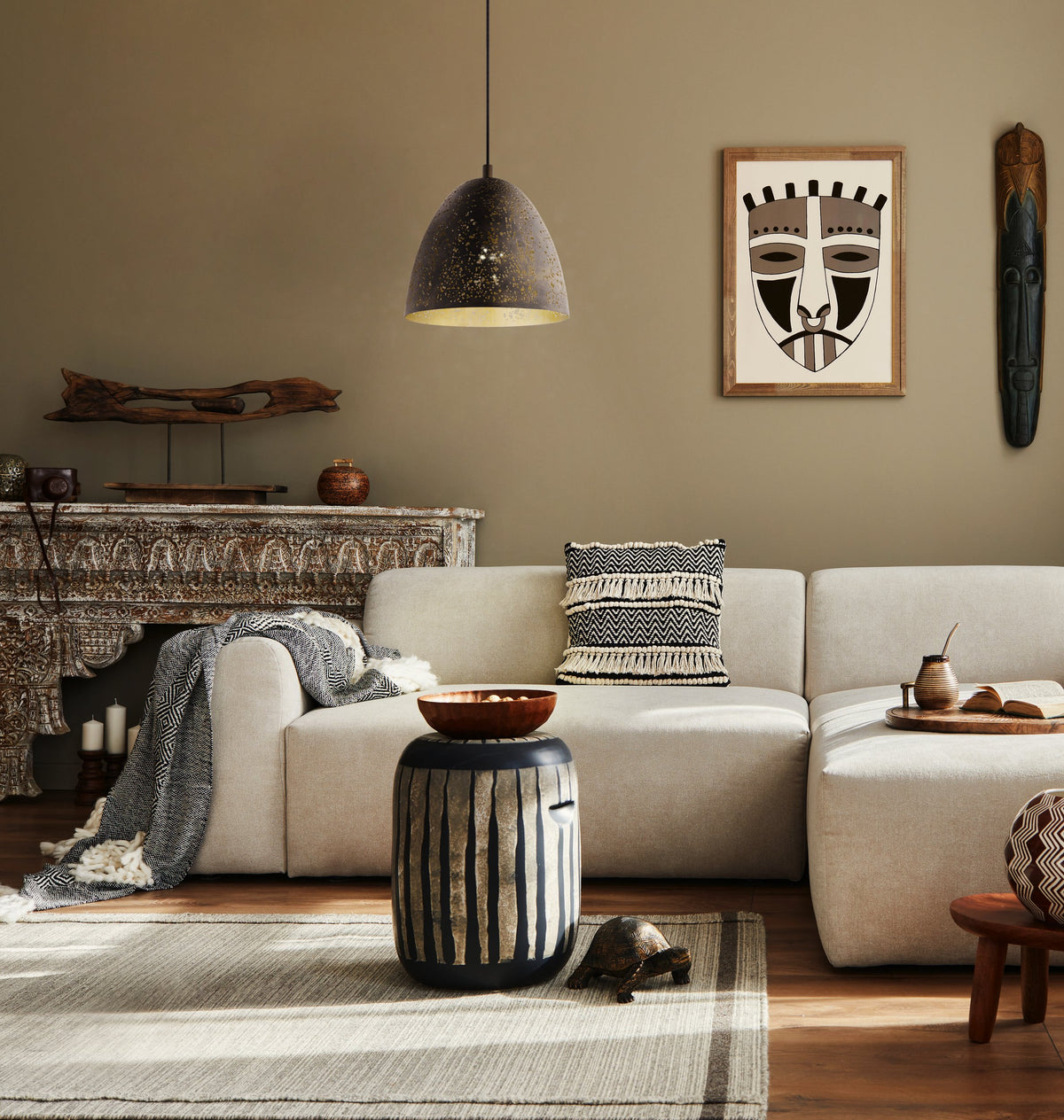 Scène de salon au décor ethnique, suspension allumée, canapé beige et coussins à motifs