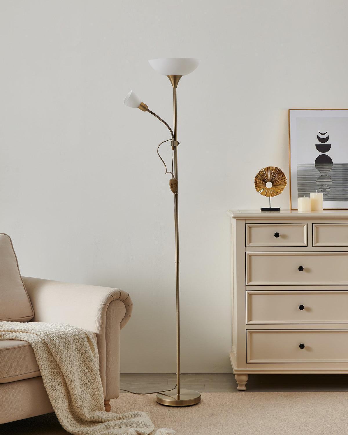 Mise en ambiance d'un lampadaire doré allumé dans un salon beige avec fauteuil.