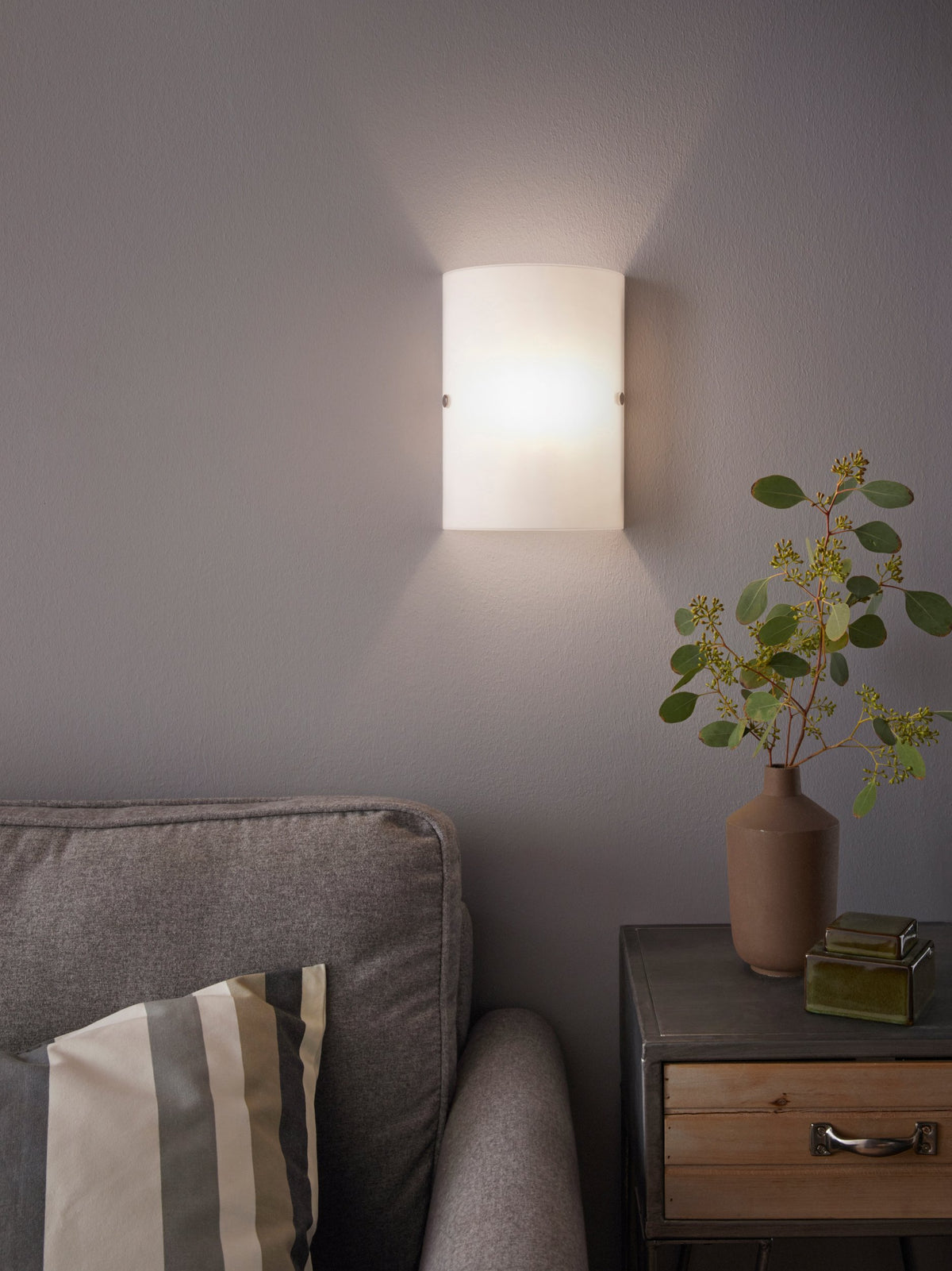 Mise en ambiance : applique allumée sur mur gris, au-dessus d'un canapé et d'une table