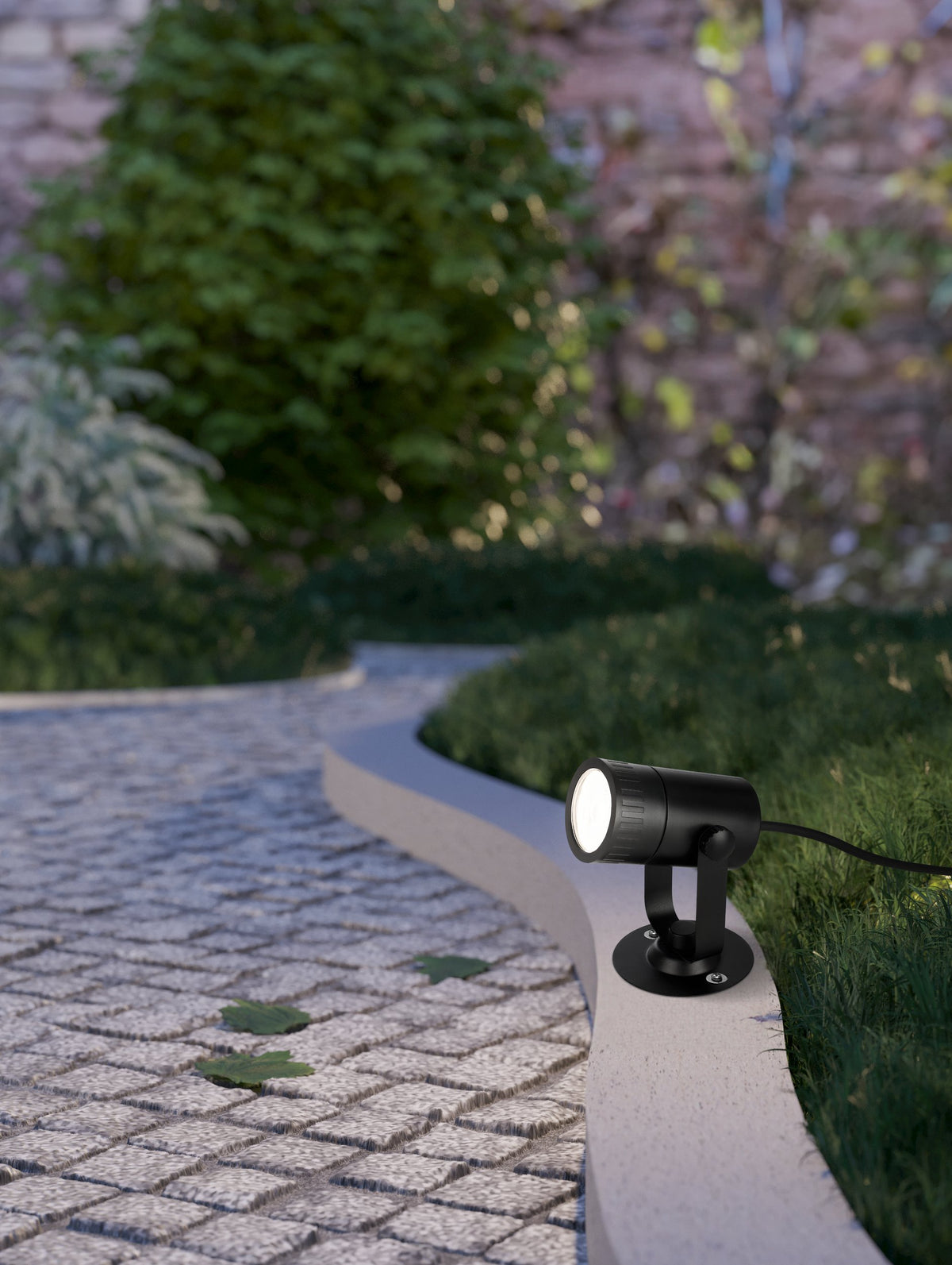 Spot extérieur noir fixé sur bordure de jardin, éclairant une allée pavée