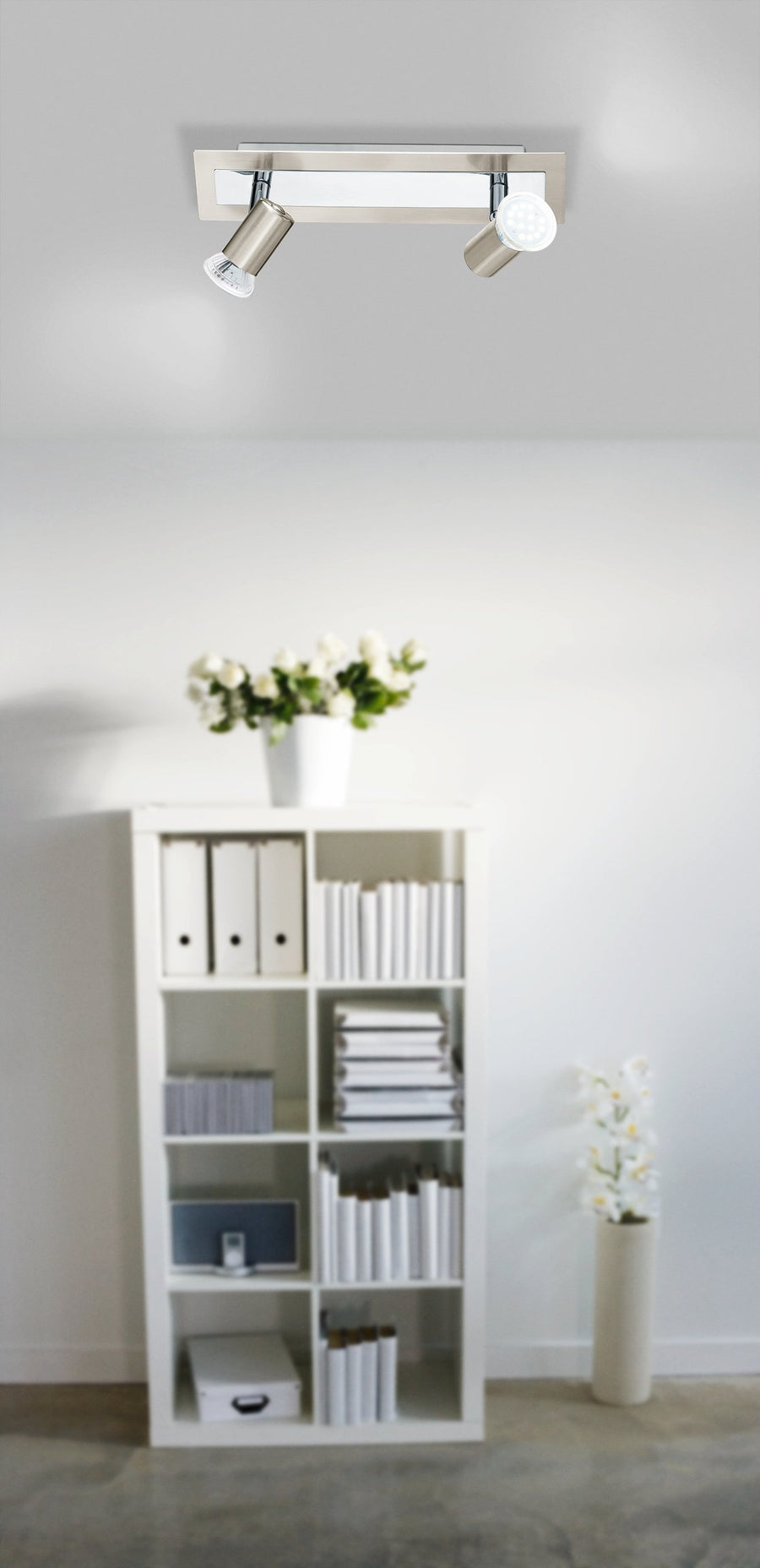 Mise en ambiance du spot plafond dans un salon blanc avec bibliothèque et fleurs.