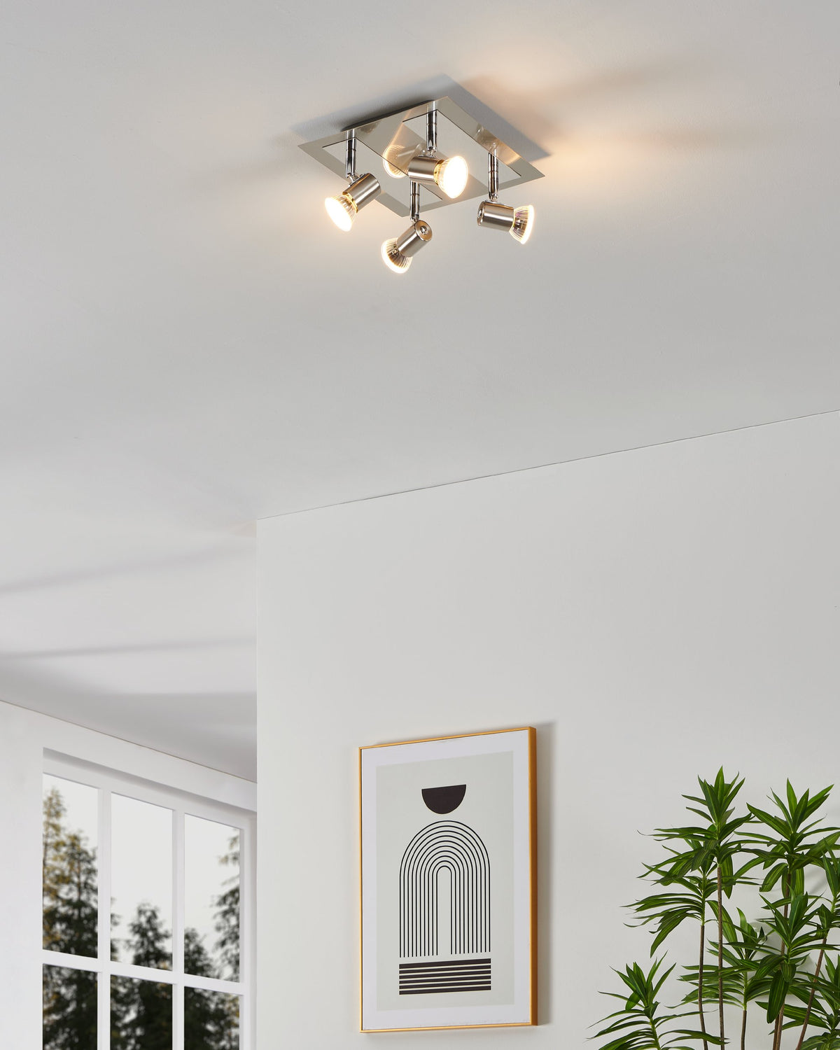 Spot installé au plafond dans un salon moderne, éclairant une pièce blanche avec cadre et plante.