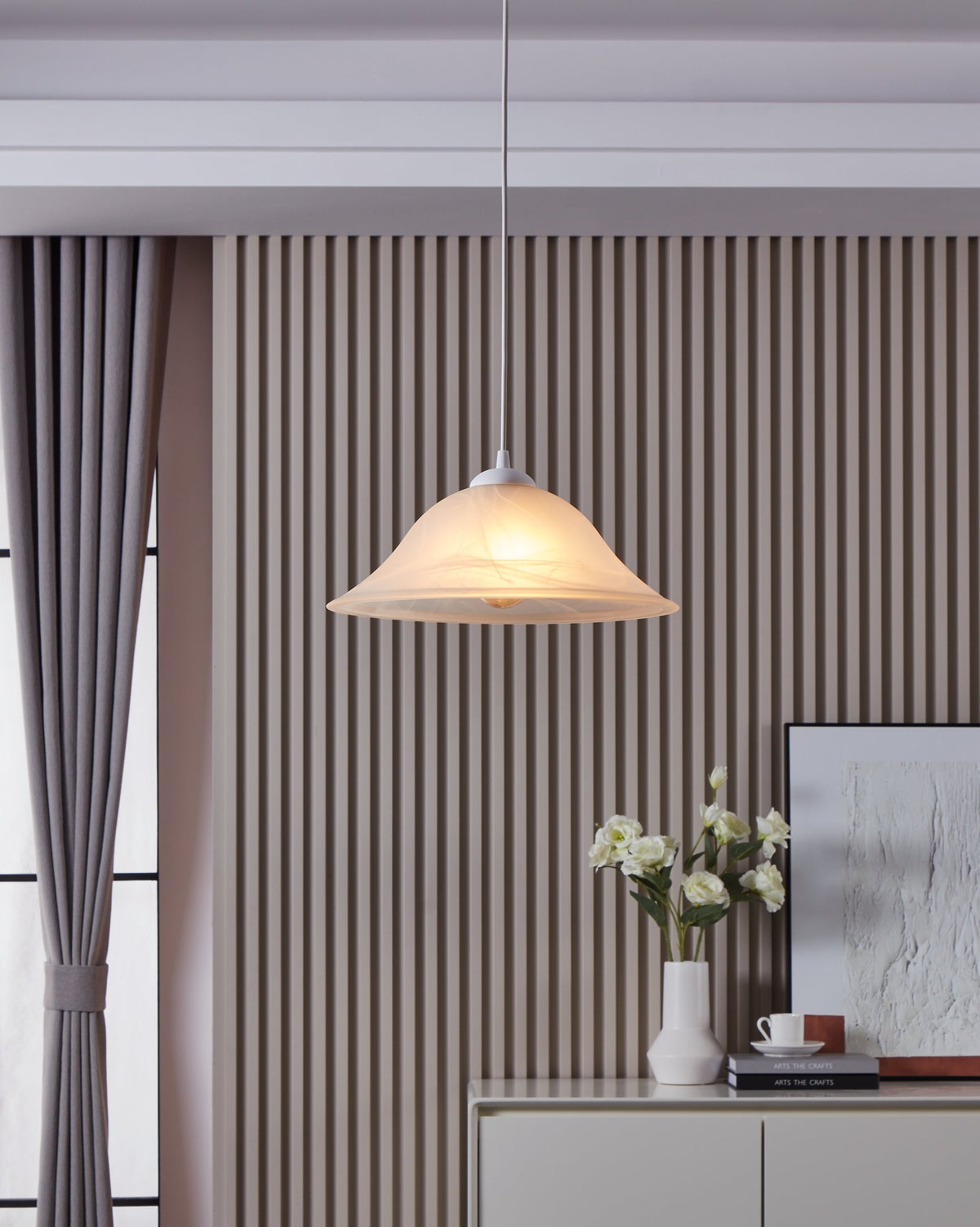 Suspension allumée dans un intérieur, au-dessus d'un buffet et d'une composition florale.