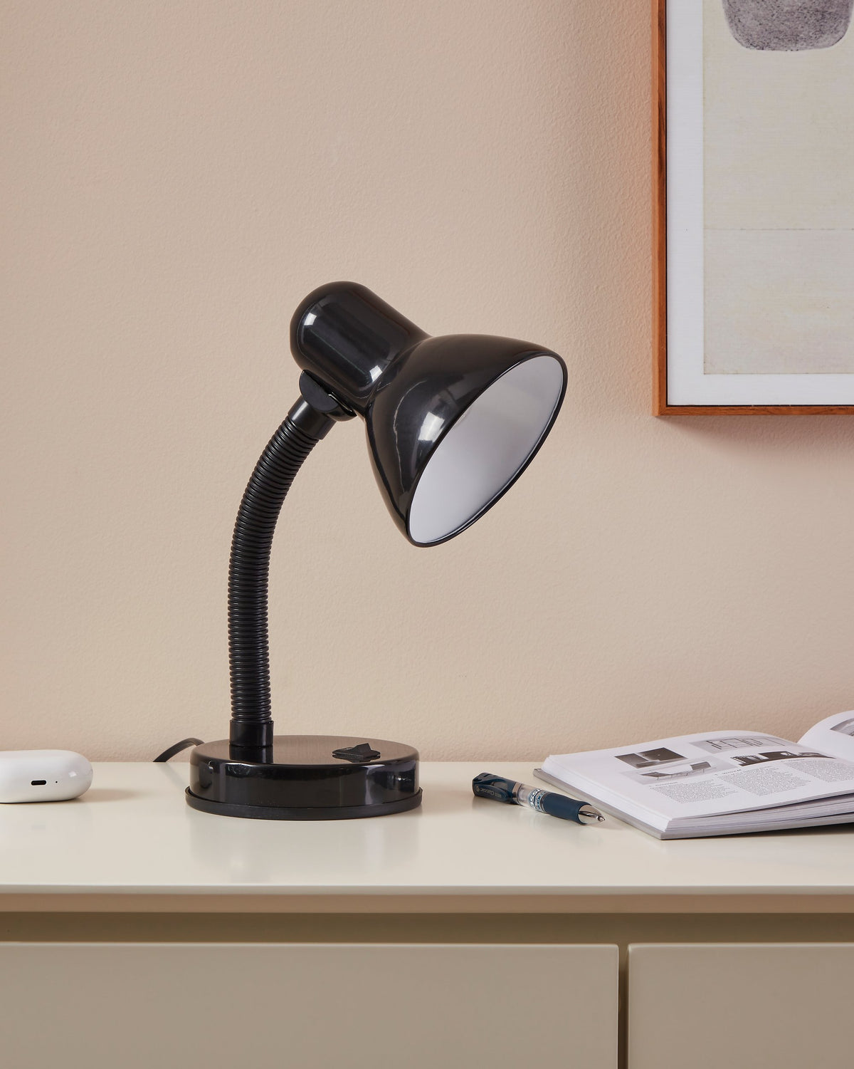 Lampe noire allumée posée sur un bureau clair, près d'un magazine et d'un stylo.