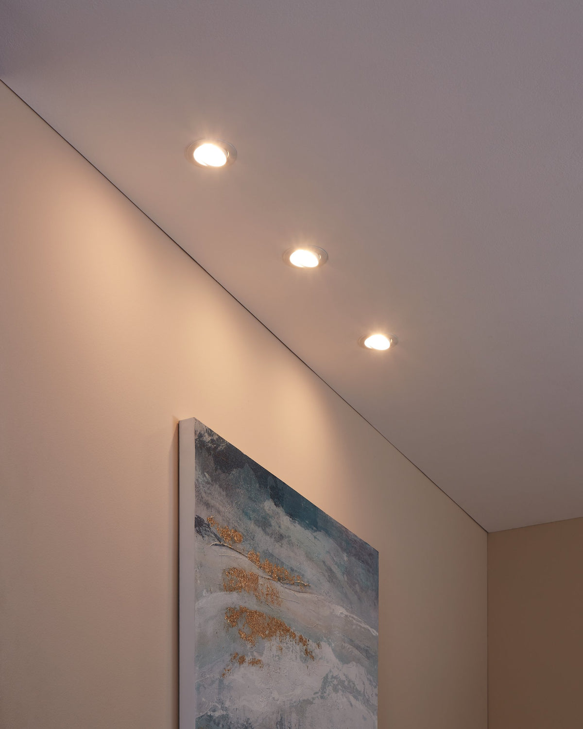 Plafond avec trois spots encastrés allumés éclairant un tableau mural