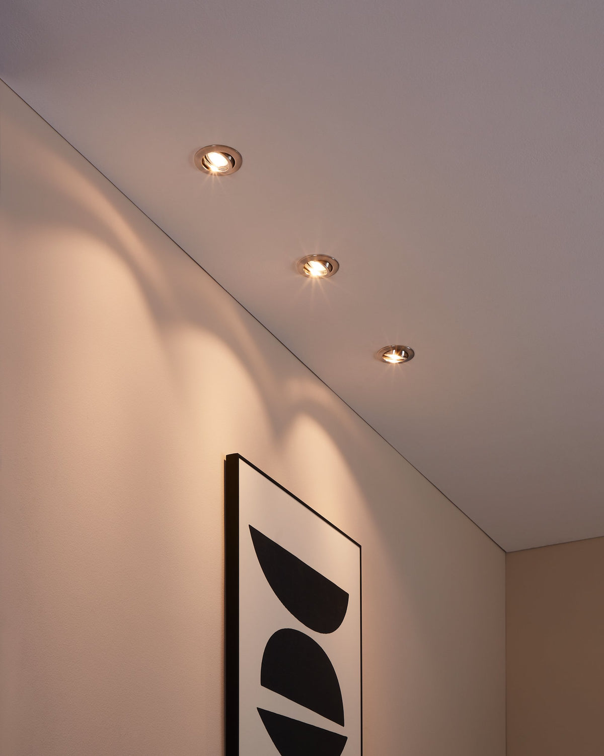 Mise en ambiance : trois spots encastrés au plafond éclairent un mur et un tableau.