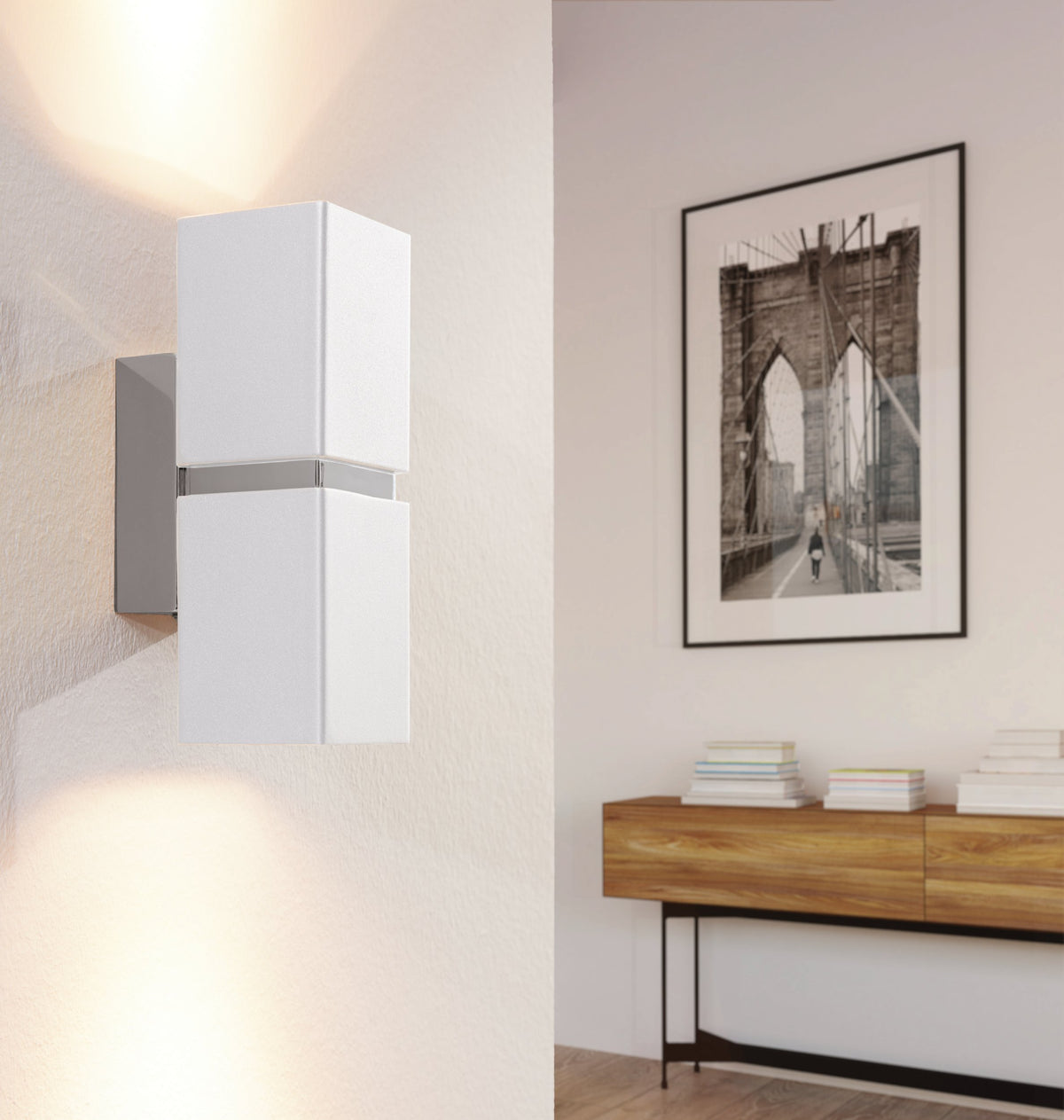 Mise en ambiance : applique allumée sur mur beige, console en bois et cadre photo.
