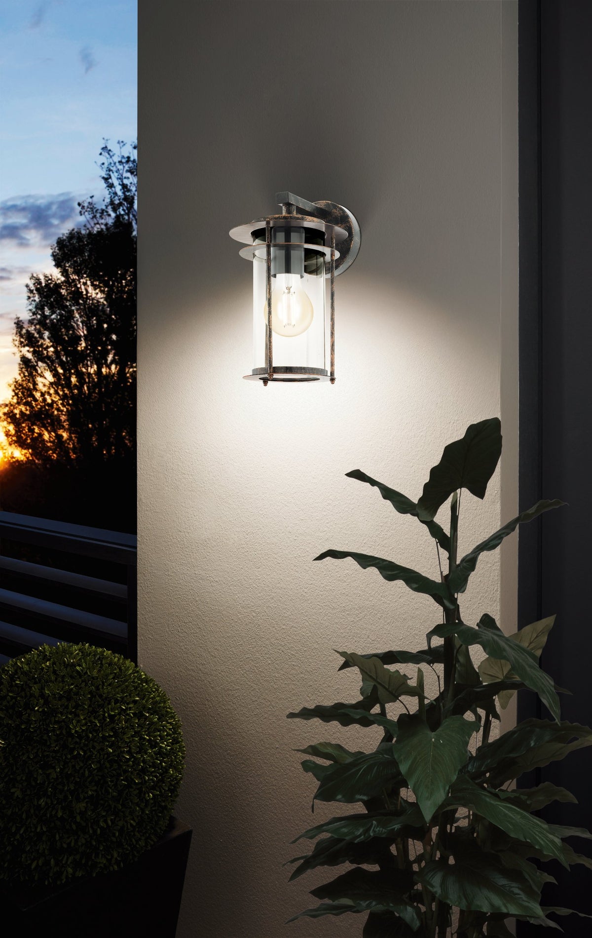 Mise en ambiance au crépuscule, applique allumée sur un mur près d'une plante verte