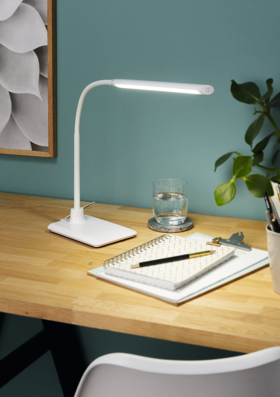 Lampe allumée sur bureau en bois devant un mur vert, ambiance travail