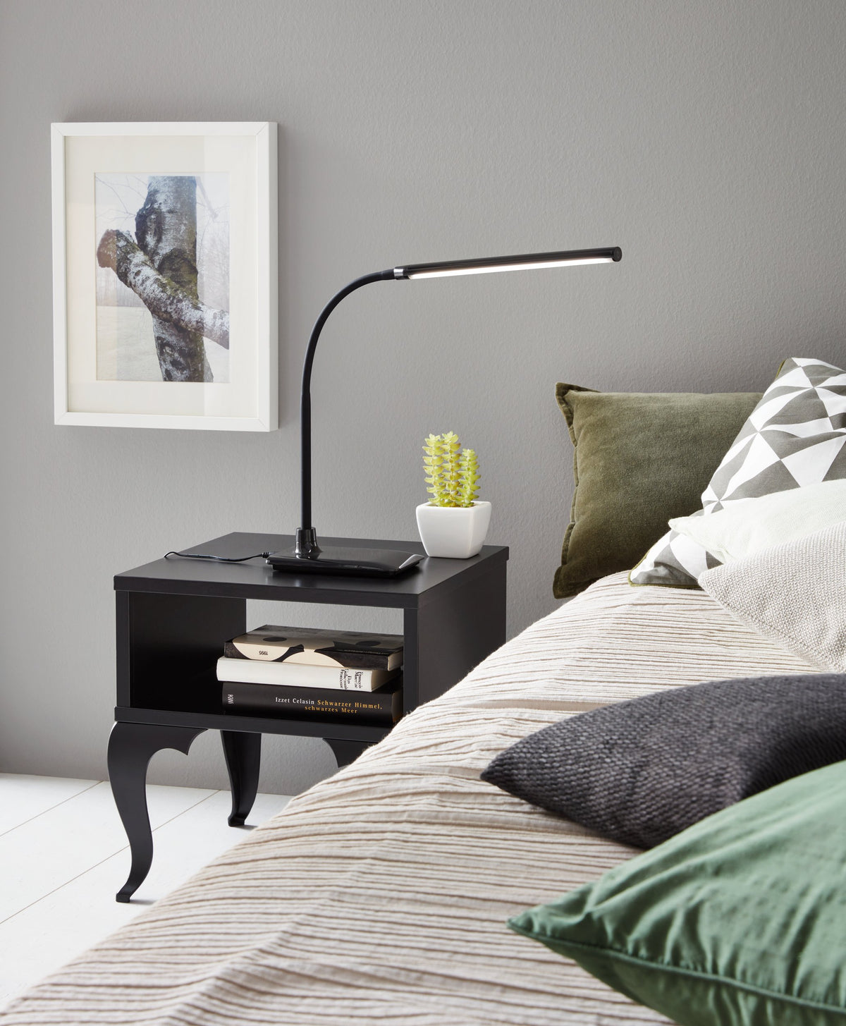 Lampe allumée sur une table de nuit, chambre avec lit, cadre et plante