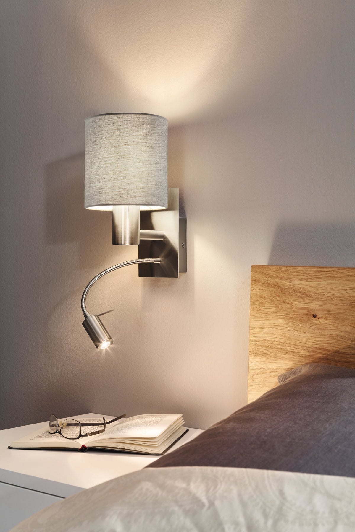 Mise en ambiance chambre : applique allumée au-dessus d'une table de nuit et d'un livre