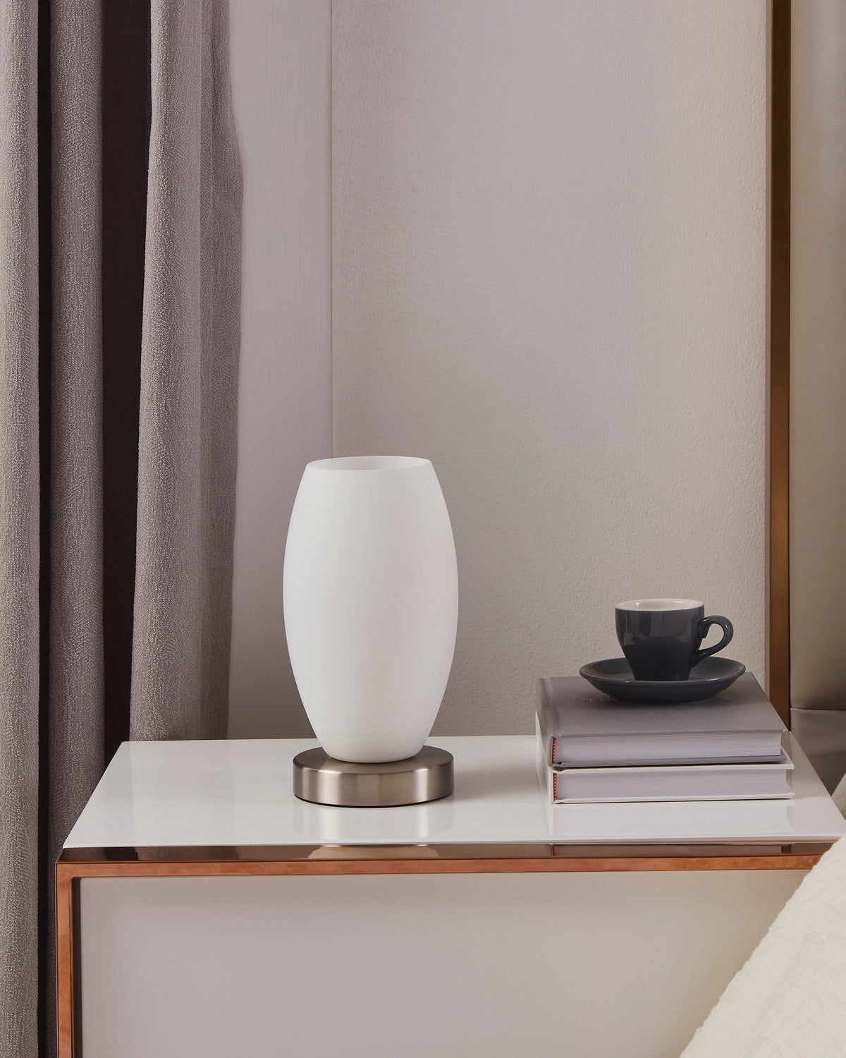 Mise en ambiance sur table de nuit, lampe allumée près d'une tasse et de livres