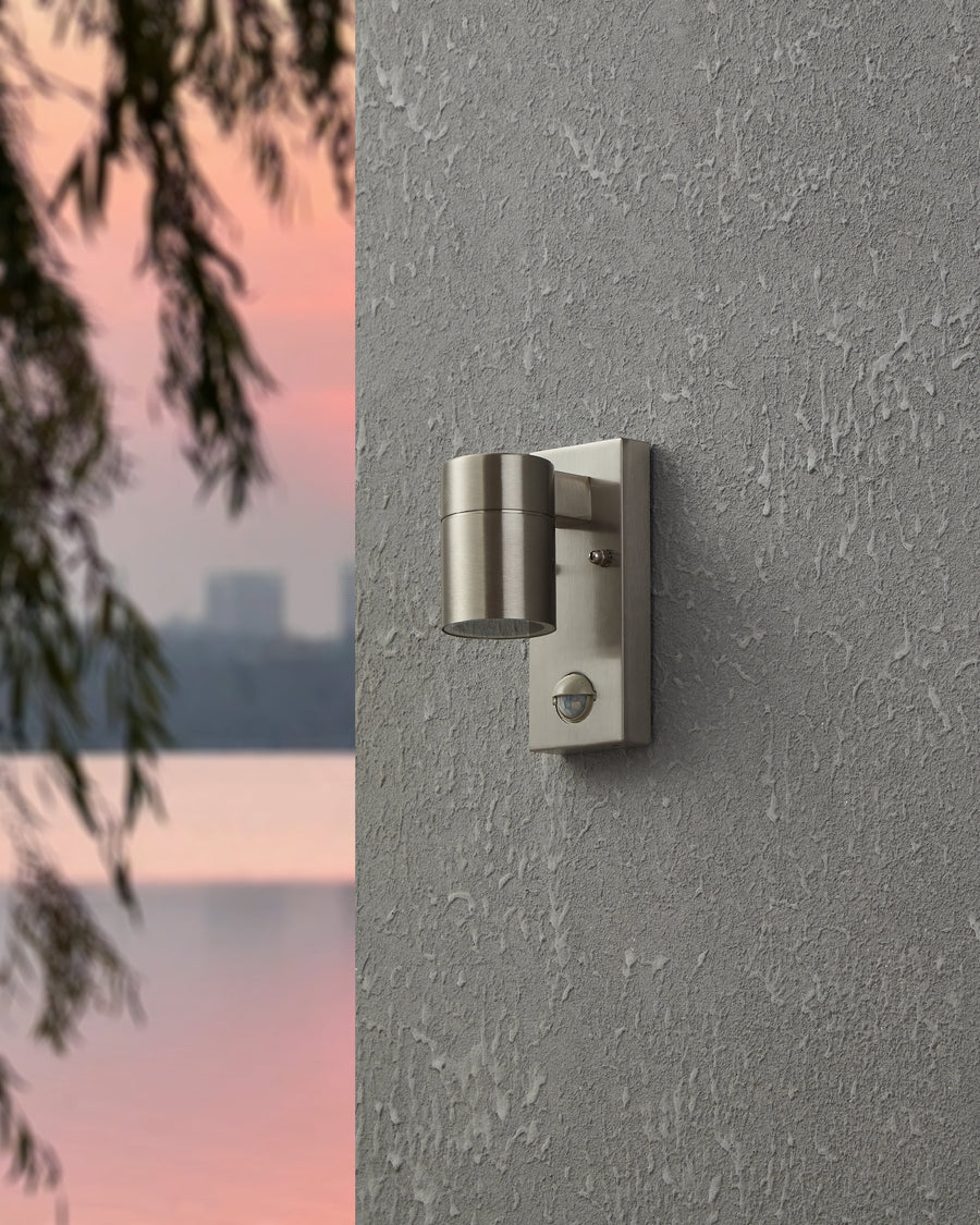 Vue de face de l'applique éteinte fixée sur une façade grise, détecteur inclus.